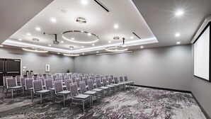 A conference room with rows of chairs, a patterned carpet, recessed ceiling lights, and a projector screen. - Holiday Inn Lubbock South by IHG (Lubbock)