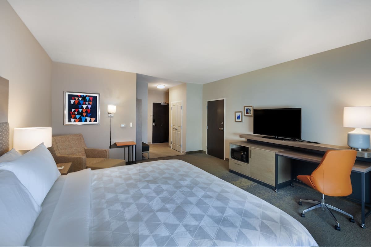 A hotel room with a large bed, a desk, a television, and a chair.