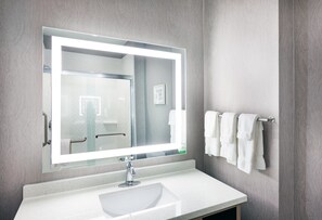 A bathroom with a large mirror, a white sink, and a towel rack with multiple towels. - Holiday Inn Lubbock South by IHG (Lubbock)