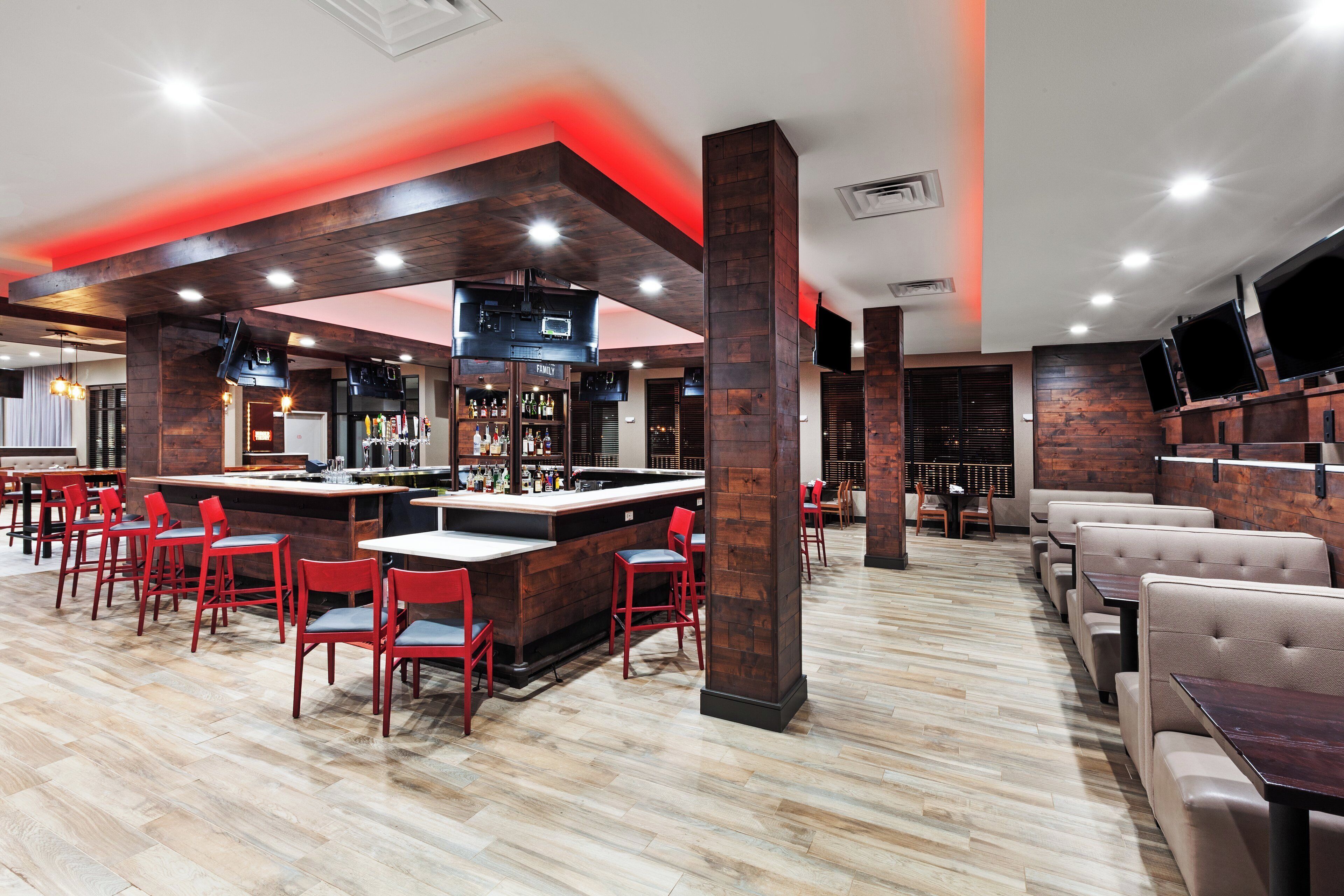 Un restaurante con zona de bar, sillas rojas y suelo de madera.