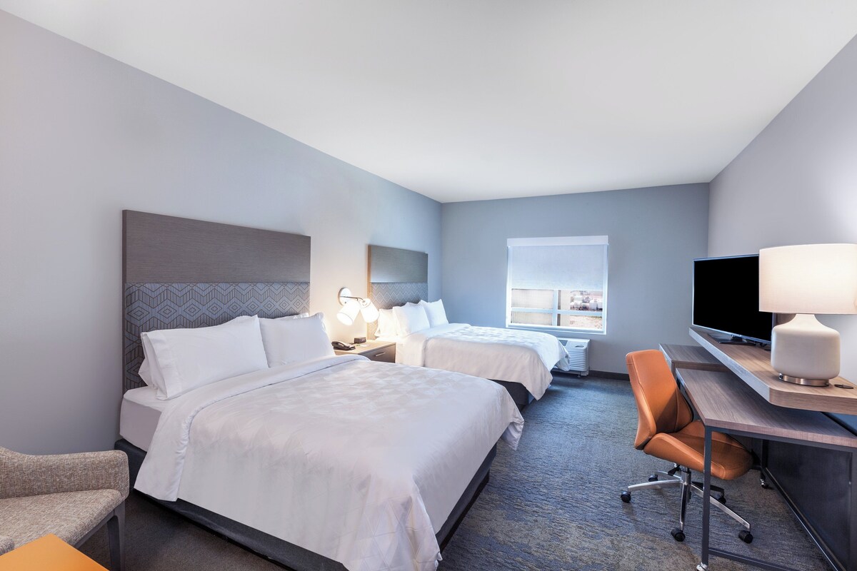 A hotel room with two beds, a desk, a chair, a TV, and a window.