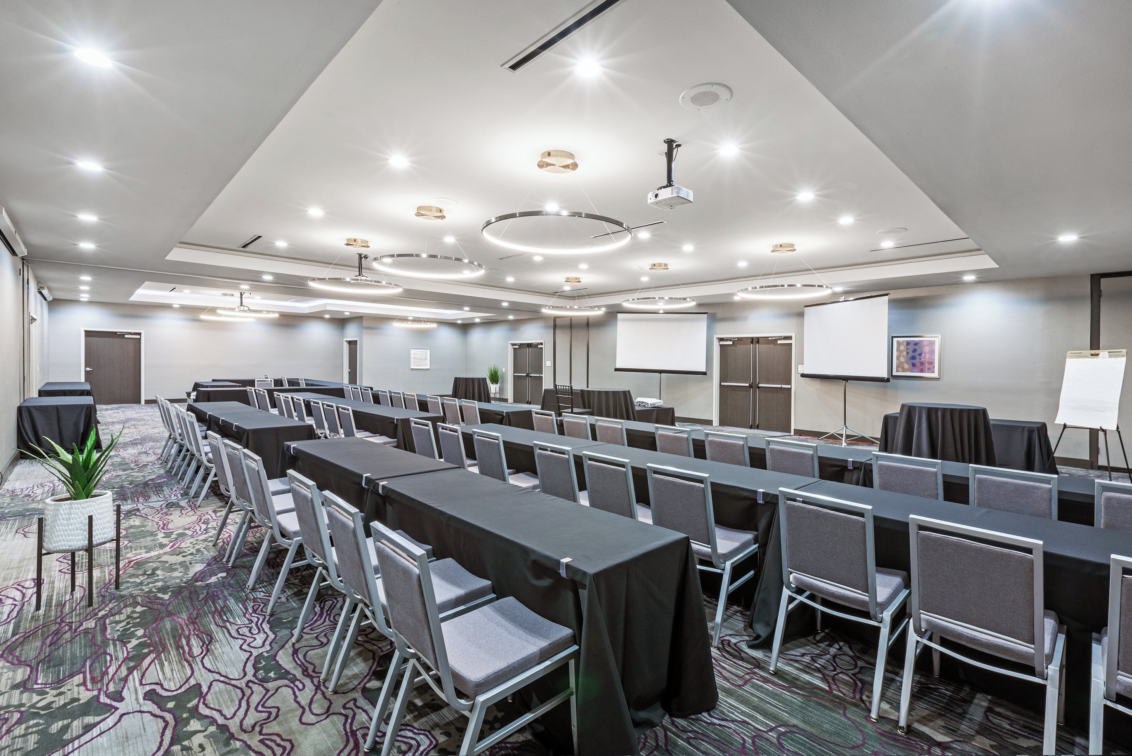 Una sala de conferencias con varias mesas y sillas, una pantalla de proyector y una pizarra.