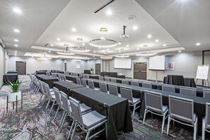 A conference room with multiple tables and chairs, a projector screen, and a whiteboard. - Holiday Inn Lubbock South by IHG (Lubbock)