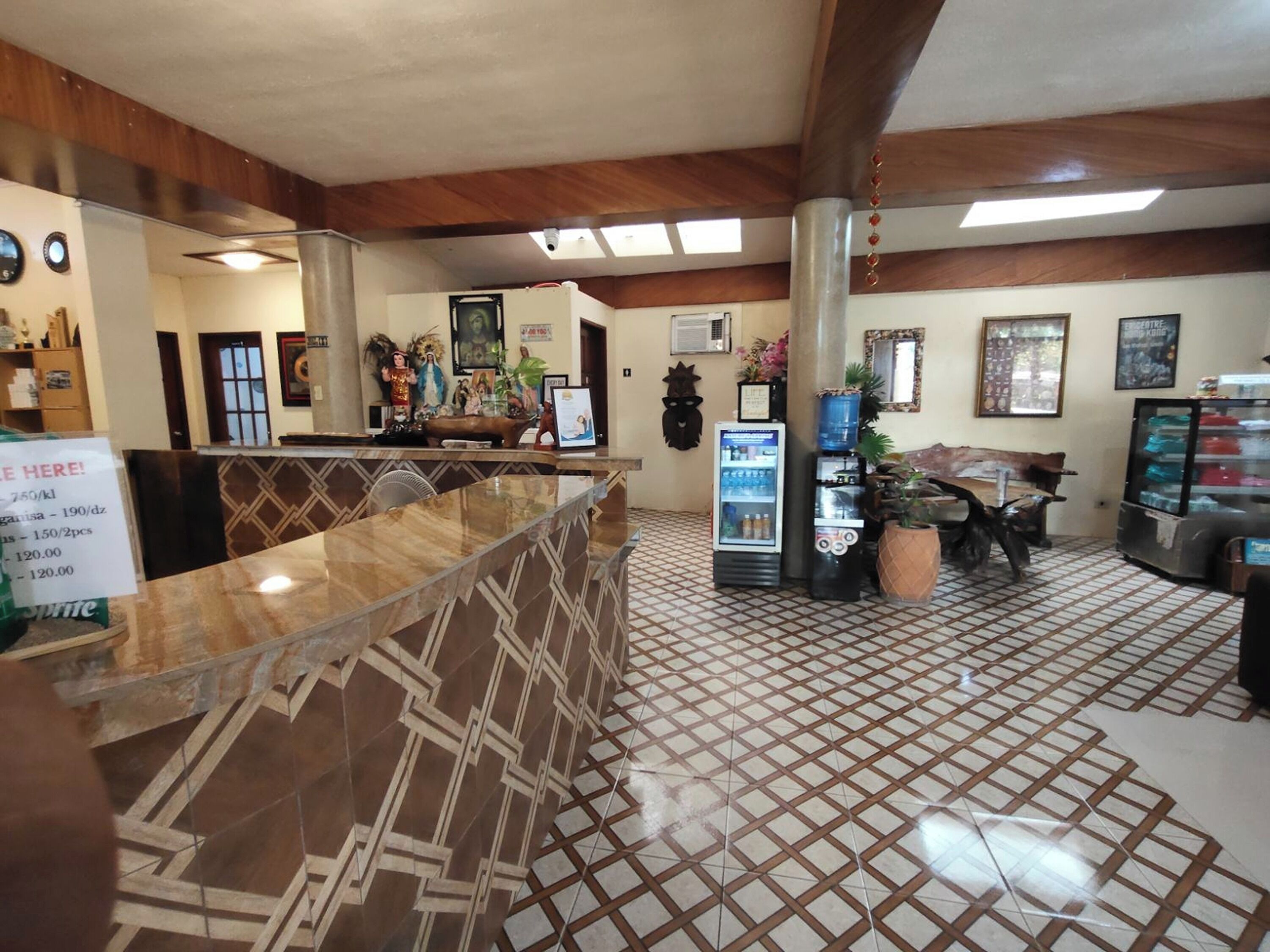 Un vestíbulo de hotel con mostrador de recepción, refrigerador, cafetera y zona de estar con mesa y sillas.