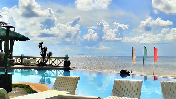 A poolside area with lounge chairs, a small bridge, and flags. - Punta Riviera Resort Bolinao (Bolinao)