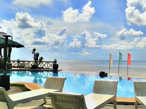 A poolside area with lounge chairs, a small bridge, and flags. - Punta Riviera Resort Bolinao (Bolinao)