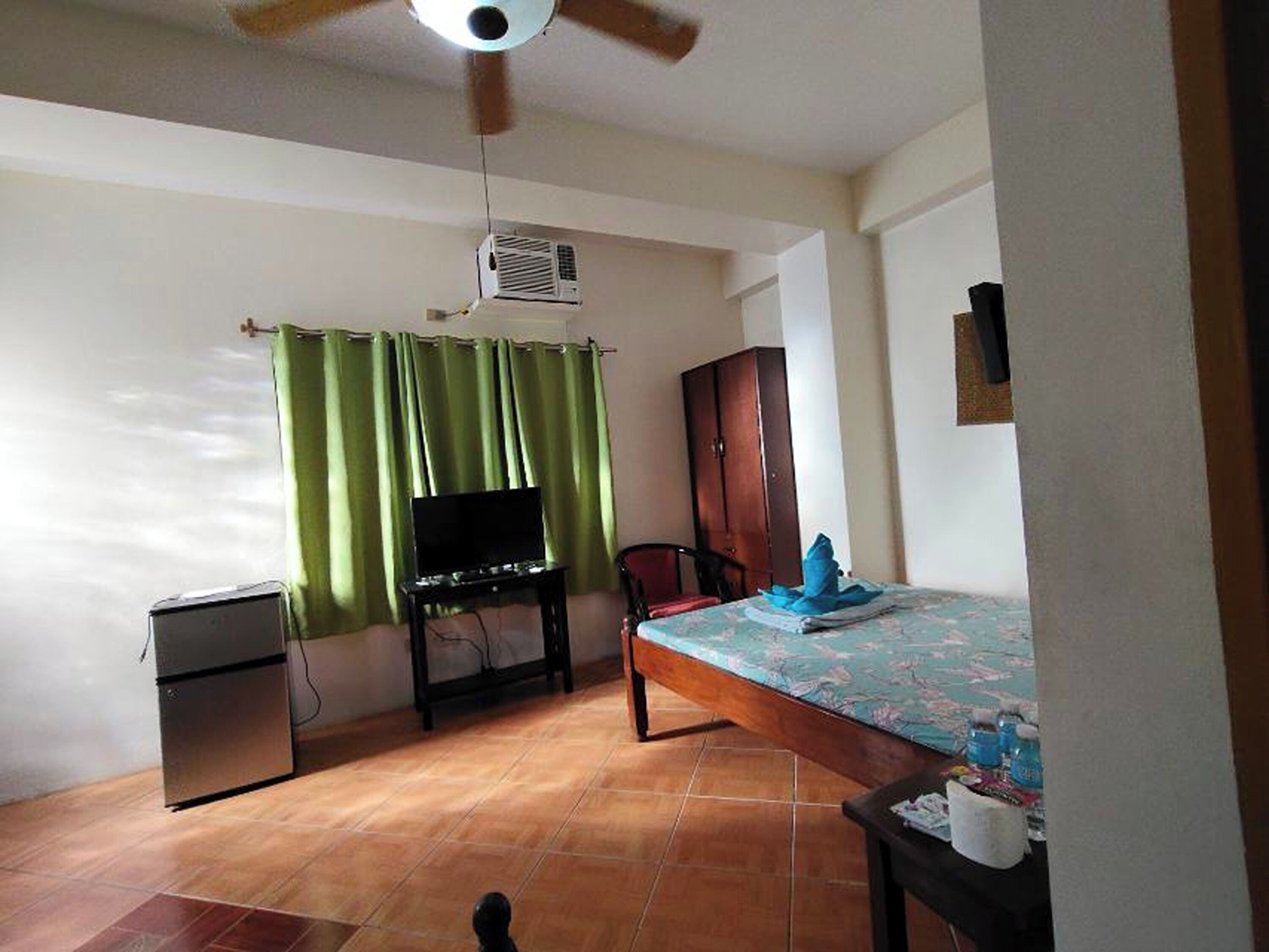 Une chambre avec un lit, une télévision, une armoire et un ventilateur de plafond.