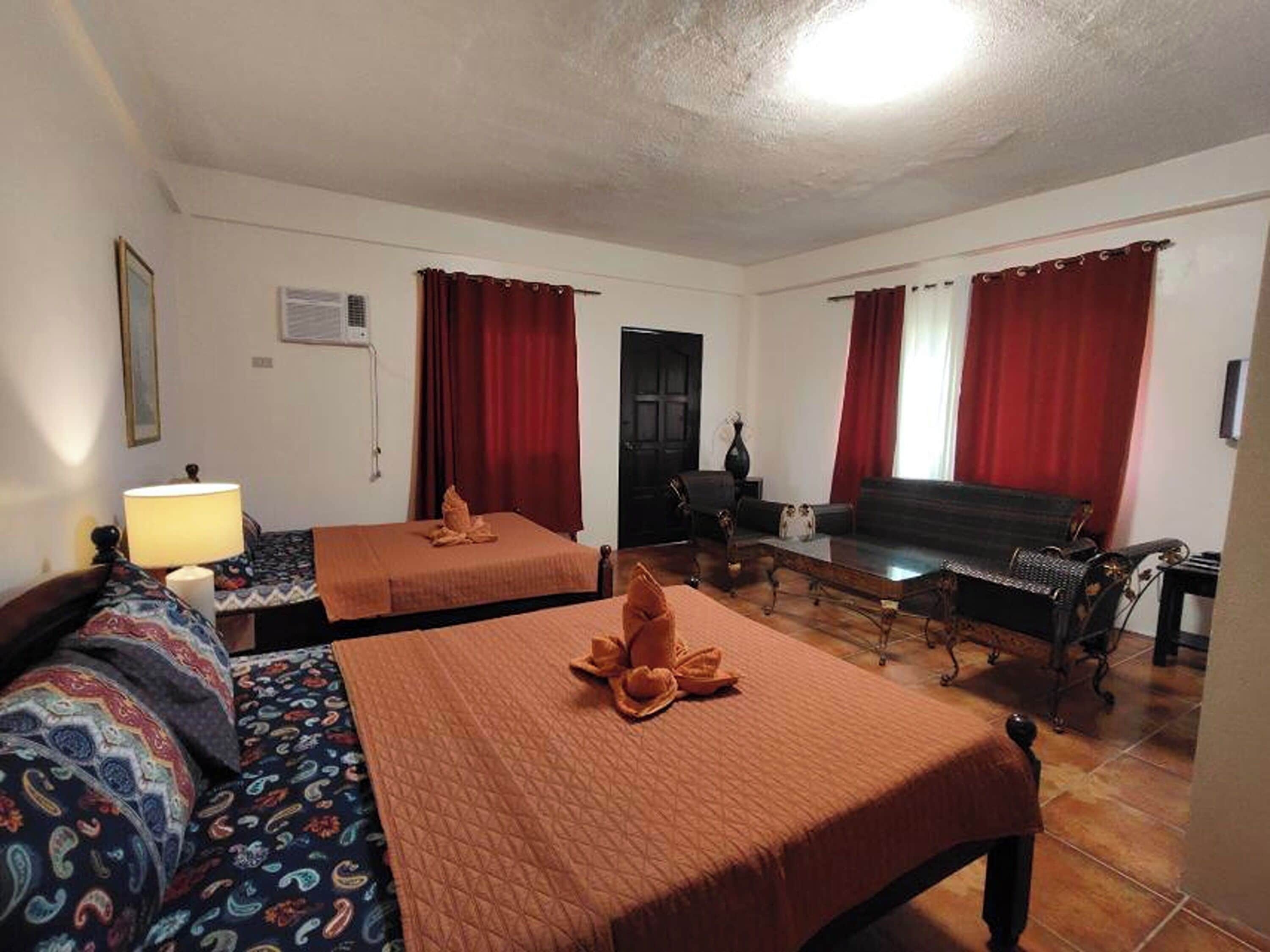 Una habitación de hotel con dos camas, un sofá, una mesa de centro de madera y cortinas rojas.