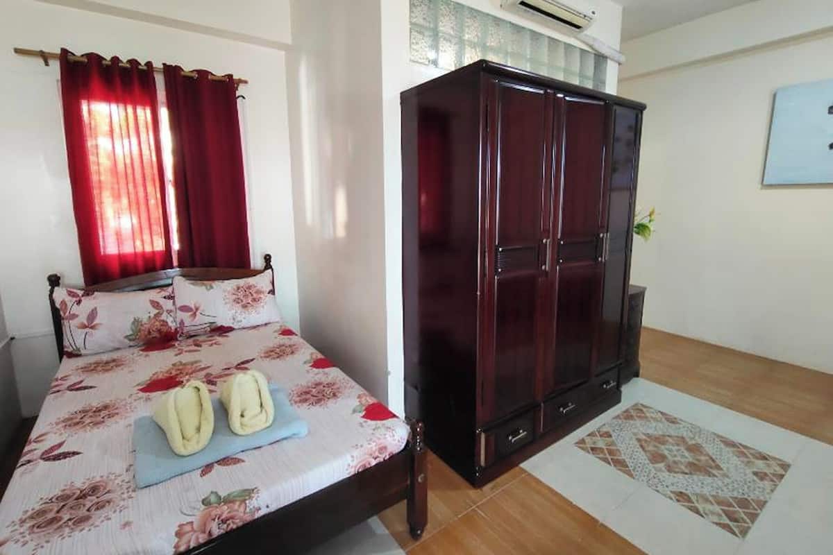 A bedroom with a bed, a wardrobe, a window with curtains, and a tiled floor.