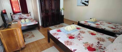 A hotel room with two beds, a wooden desk, a wardrobe, and a painting on the wall.