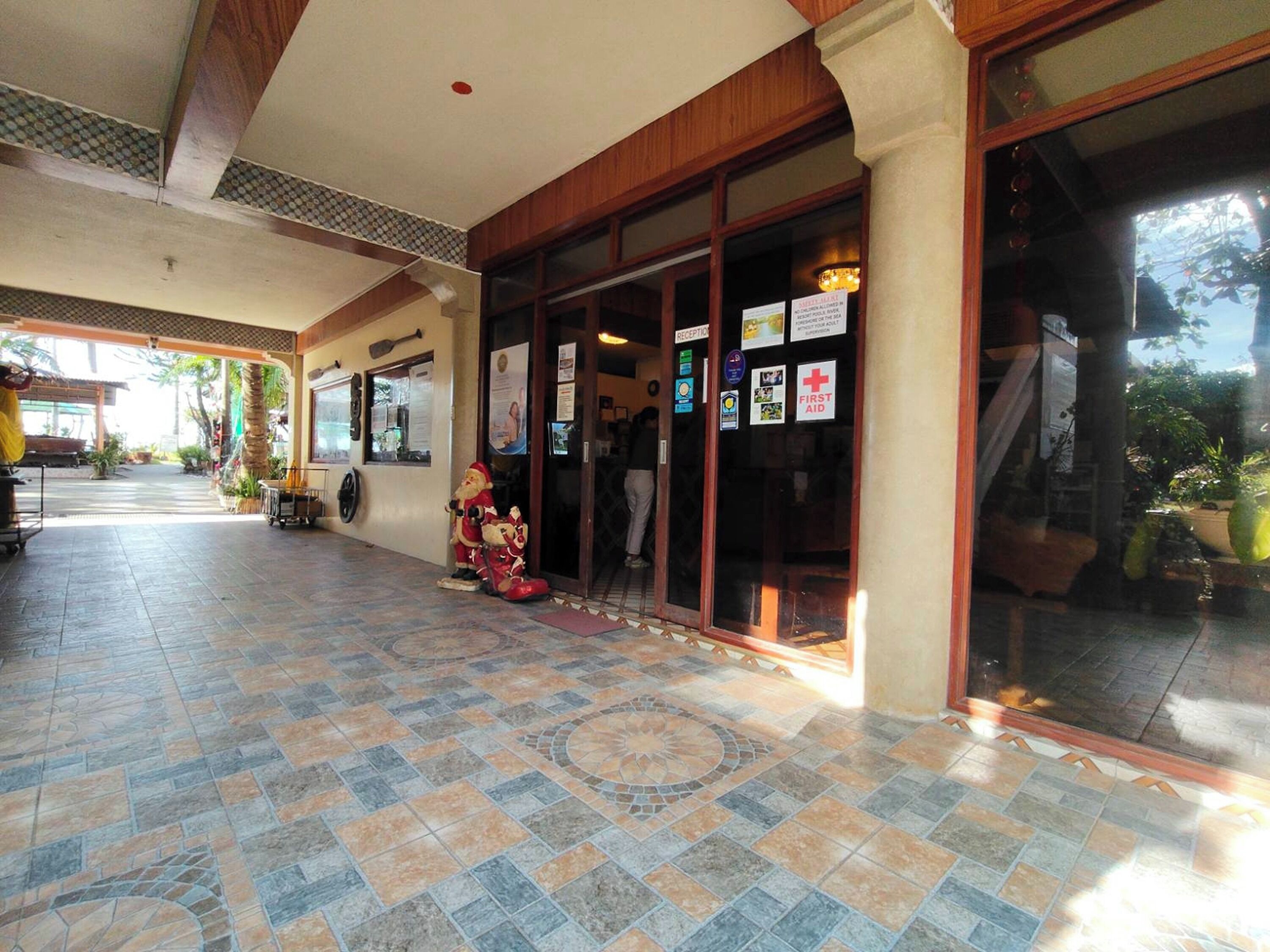 A hotel entrance with a tiled floor, a reception desk, and a Santa statue outside.