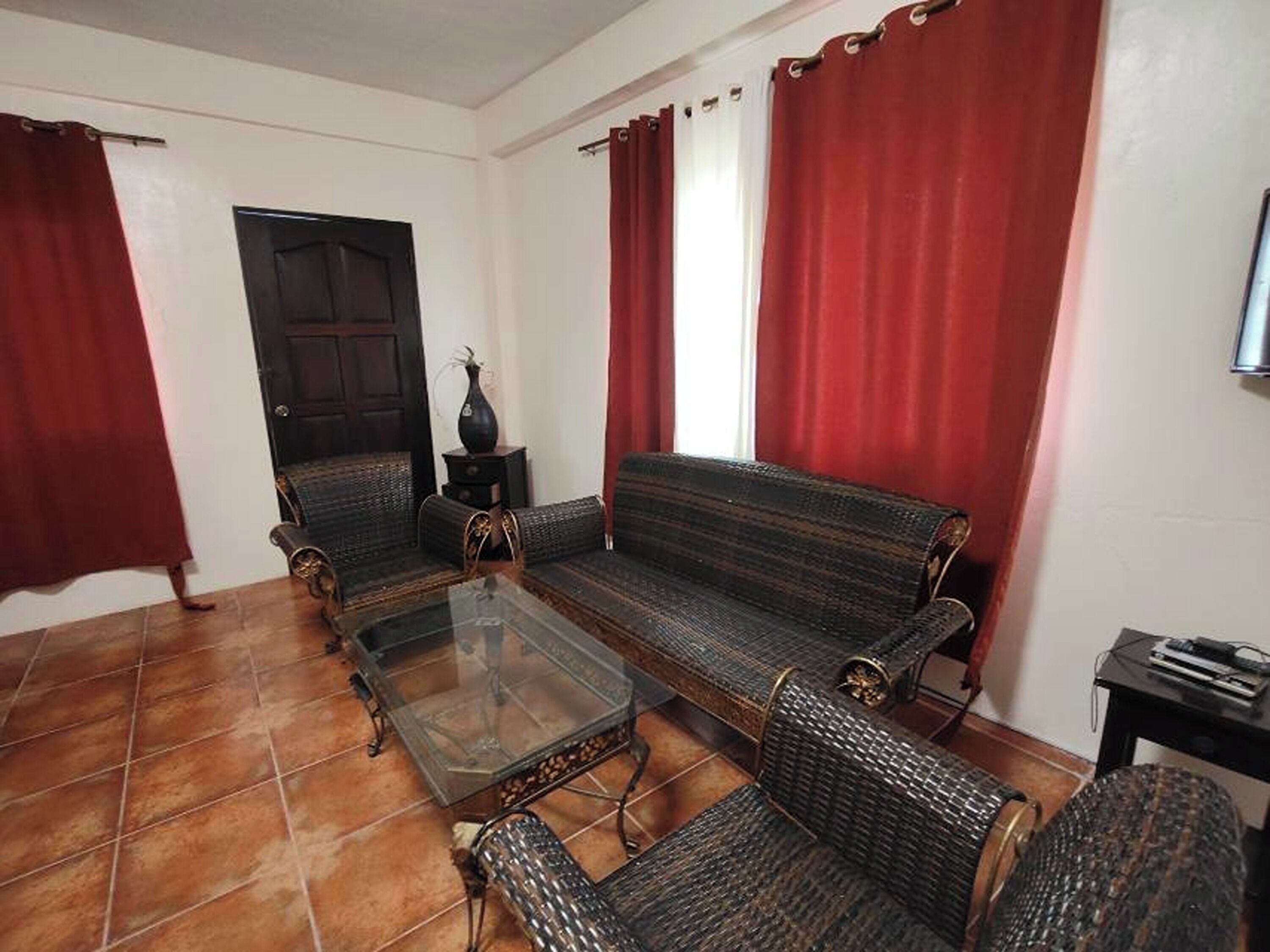 A living room with a sofa, armchairs, a glass coffee table, and a small side table with a vase.