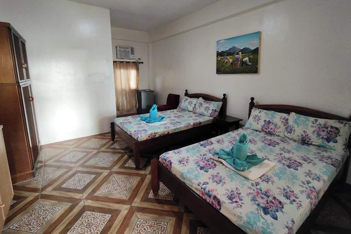 A room with two beds, a wooden wardrobe, a painting on the wall, and an air conditioning unit.