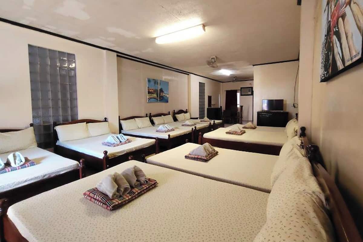 A hotel room with four single beds, a sofa, a TV, and a painting on the wall.