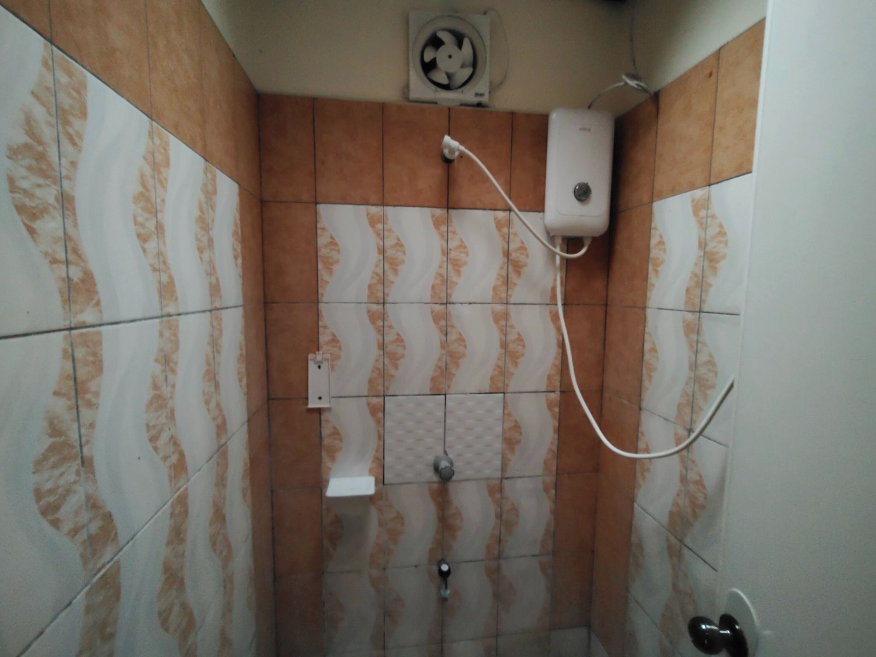 A bathroom with patterned tiles, a white pedestal sink, a handheld showerhead, and a wall-mounted fan.