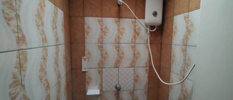 Ein Badezimmer mit gemusterten Fliesen, einem weißen Waschbecken auf Säule, einer Handbrause und einem Wandventilator.