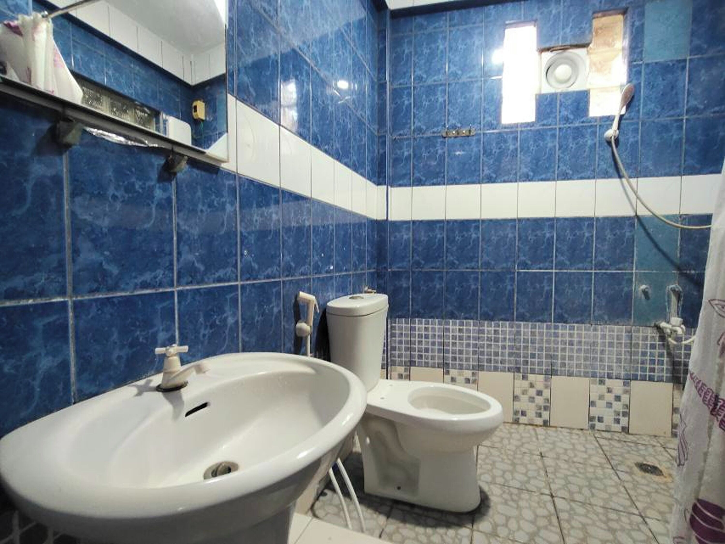 A bathroom with blue marble tiles, a white sink, a toilet, and a shower area.