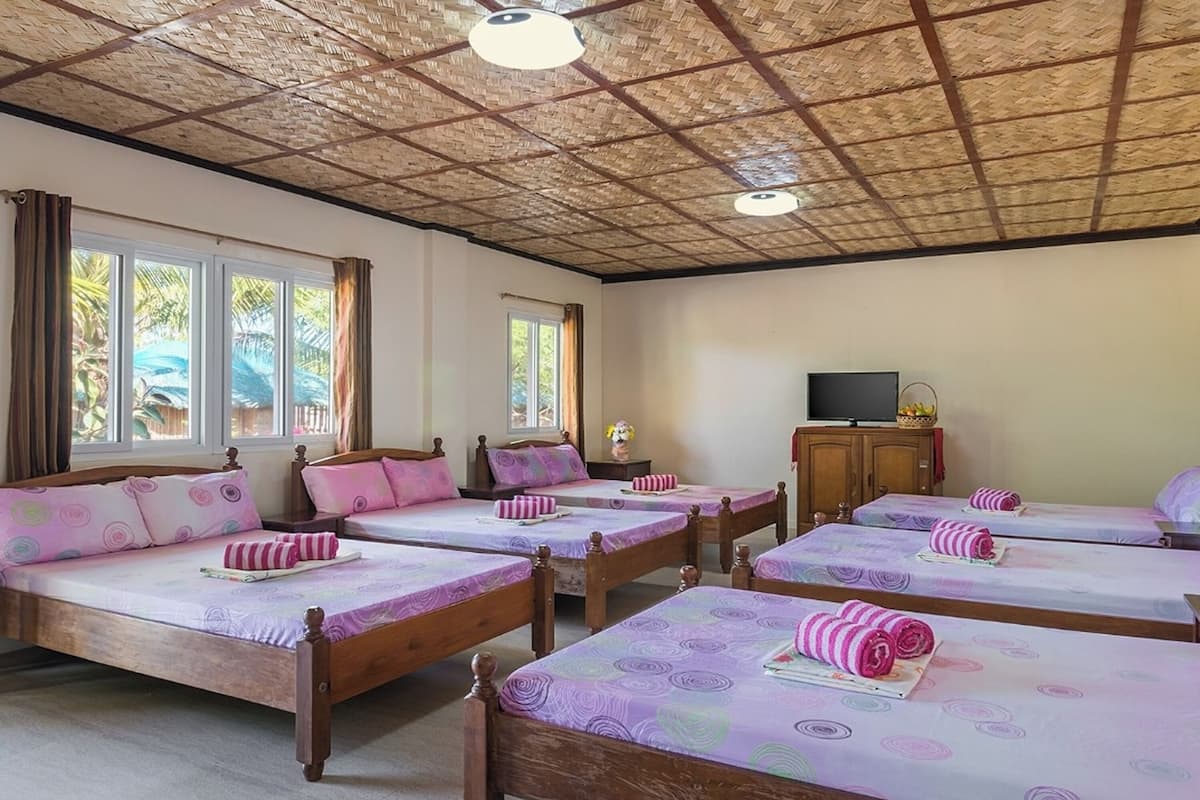 A hotel room with four wooden beds, each with a purple and pink patterned bedspread, and a television on a wooden cabinet.