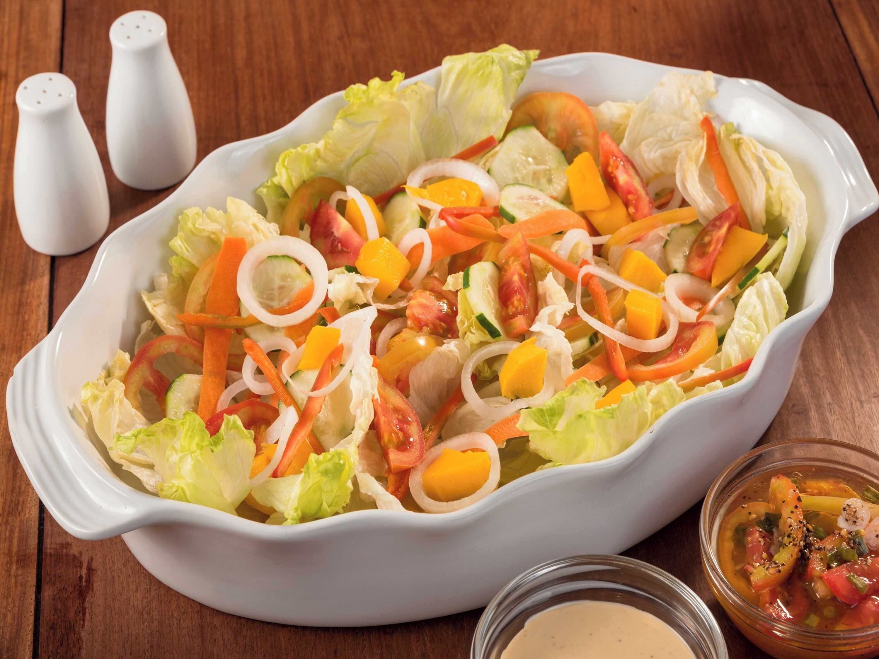 A white oval dish filled with a colorful salad on a wooden table.