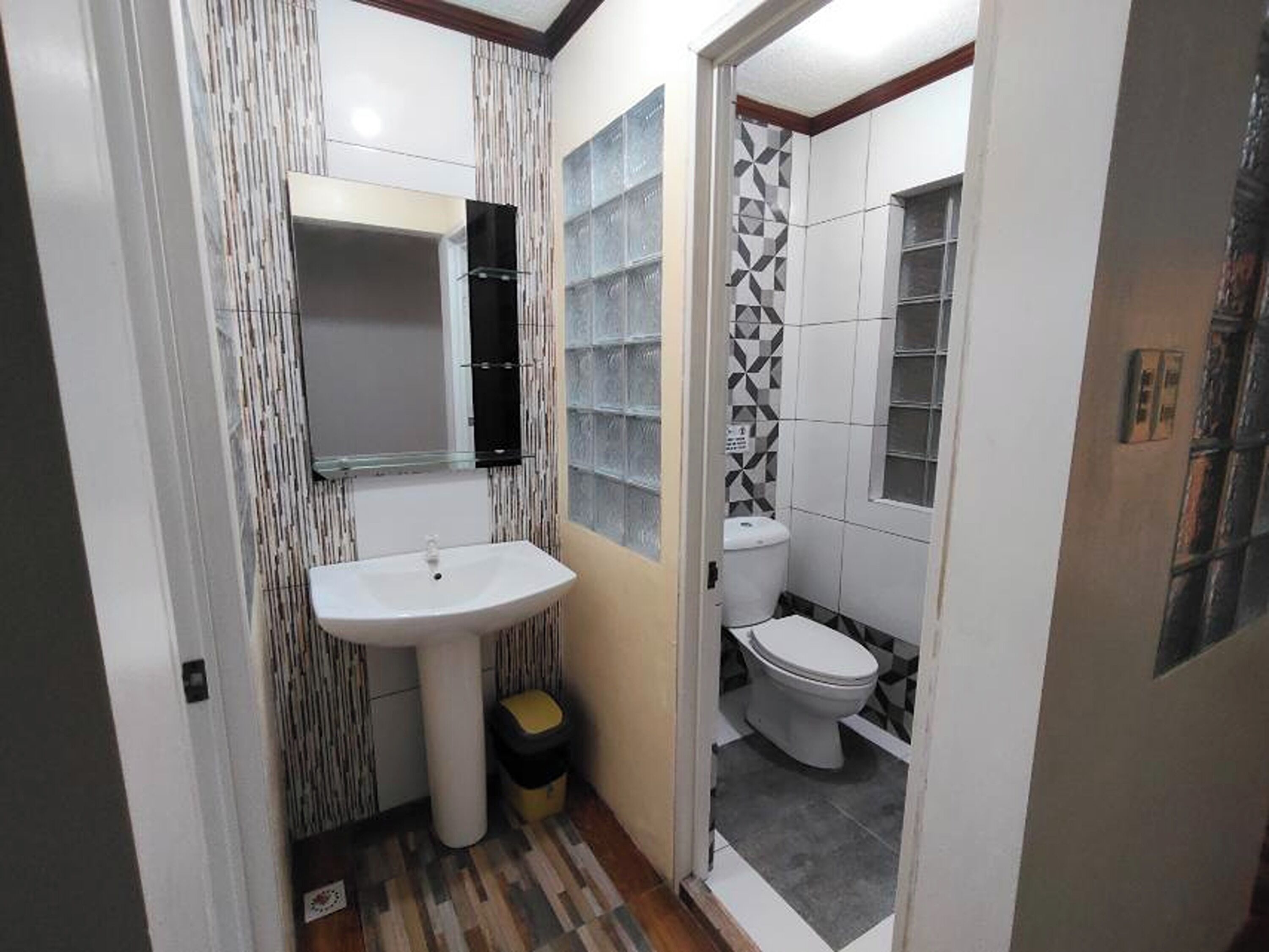 Un baño pequeño con lavamanos blanco, espejo y retrete.