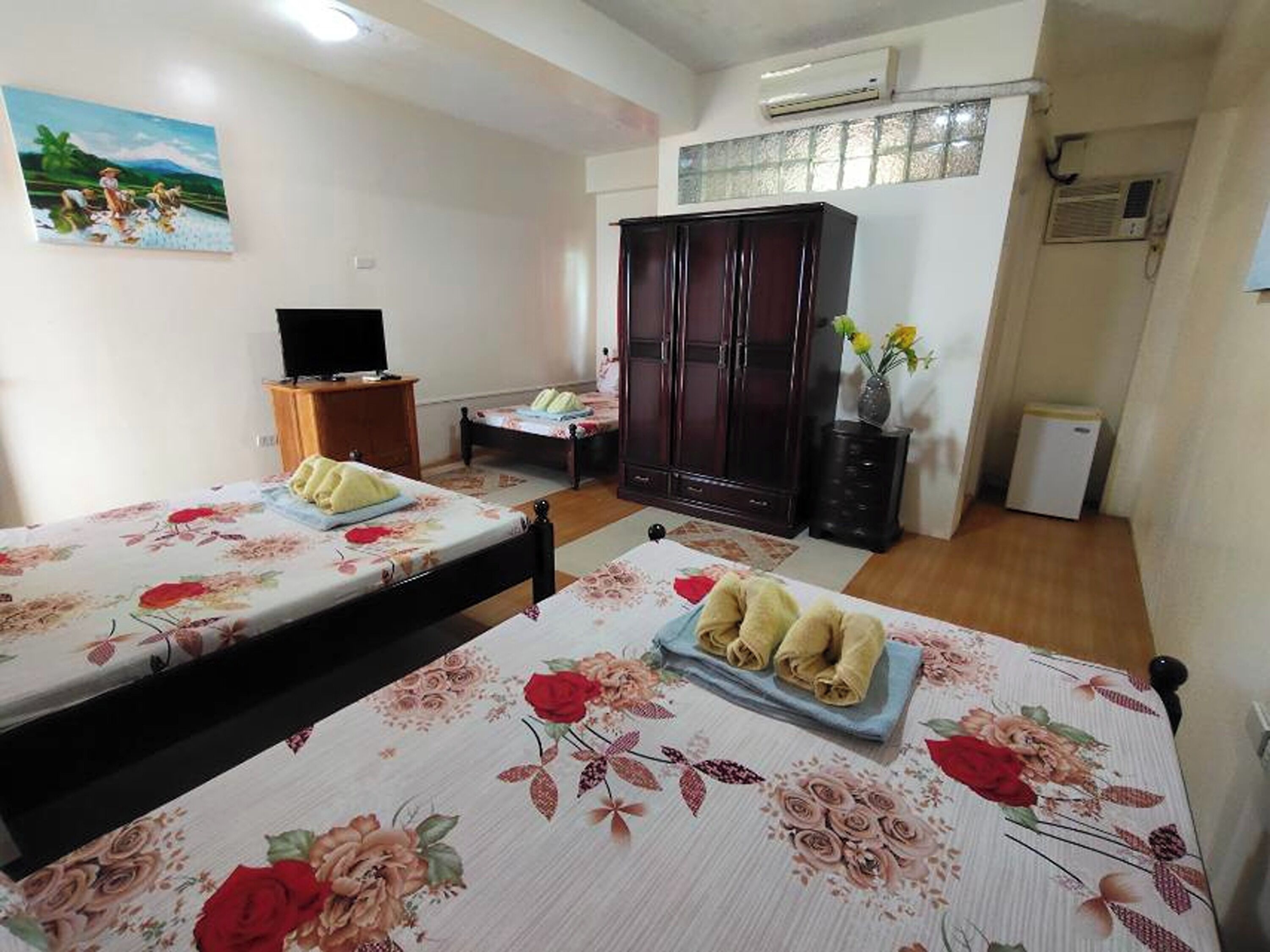 A hotel room with two beds, a wardrobe, a television, and a small table.