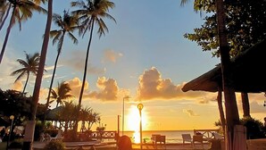 A sunset view from a resort with palm trees, a beach, and lounge chairs. - Punta Riviera Resort Bolinao (Bolinao)