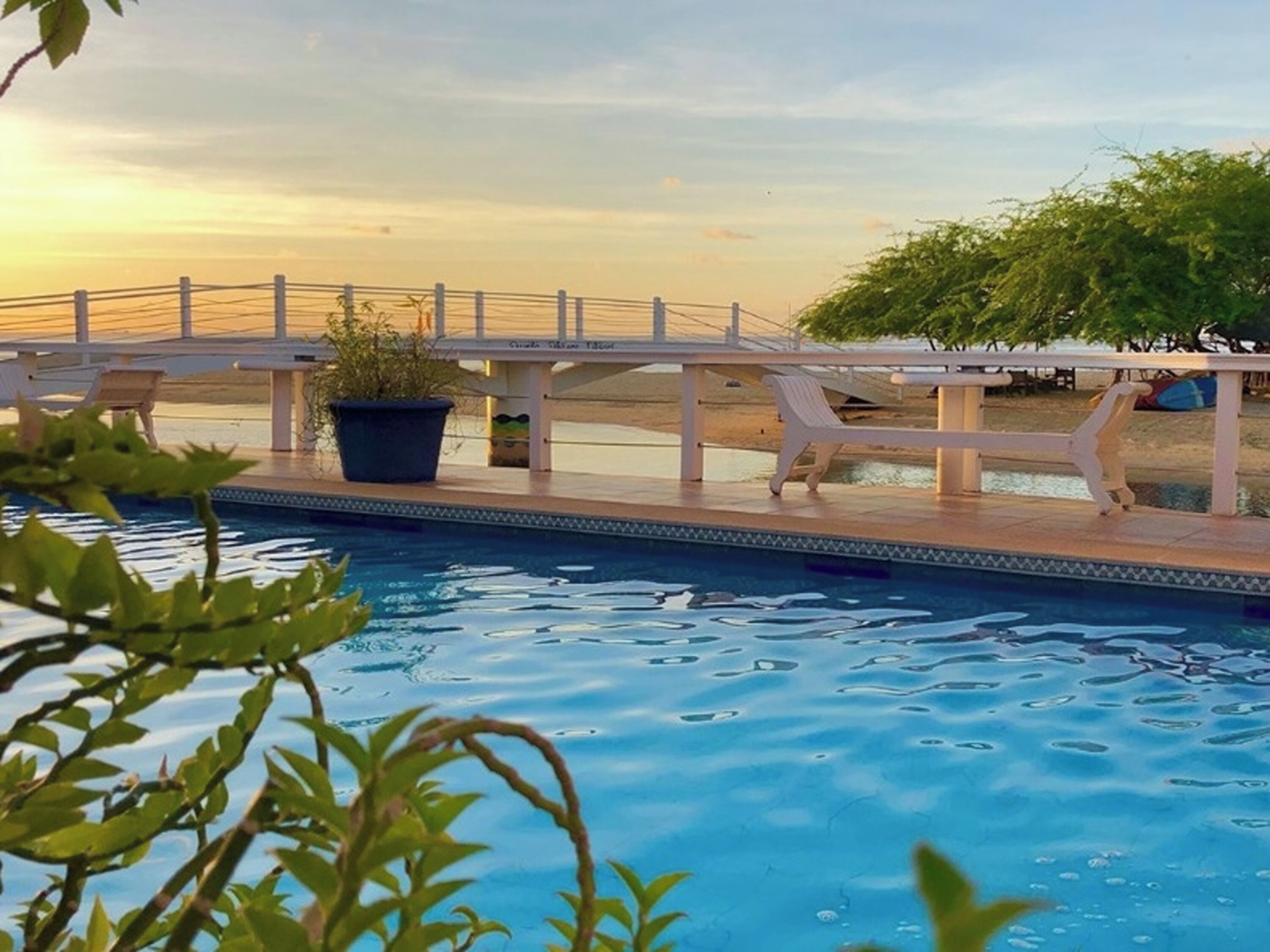 Un área de piscina con terraza blanca, sillas de descanso y un puente.