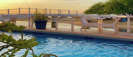 Un área de piscina con terraza blanca, sillas de descanso y un puente.