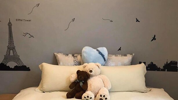 A bed with a teddy bear, pillows, and a wall decal of the Eiffel Tower and birds. - Tainan Jie Guo Inn (Tainan)
