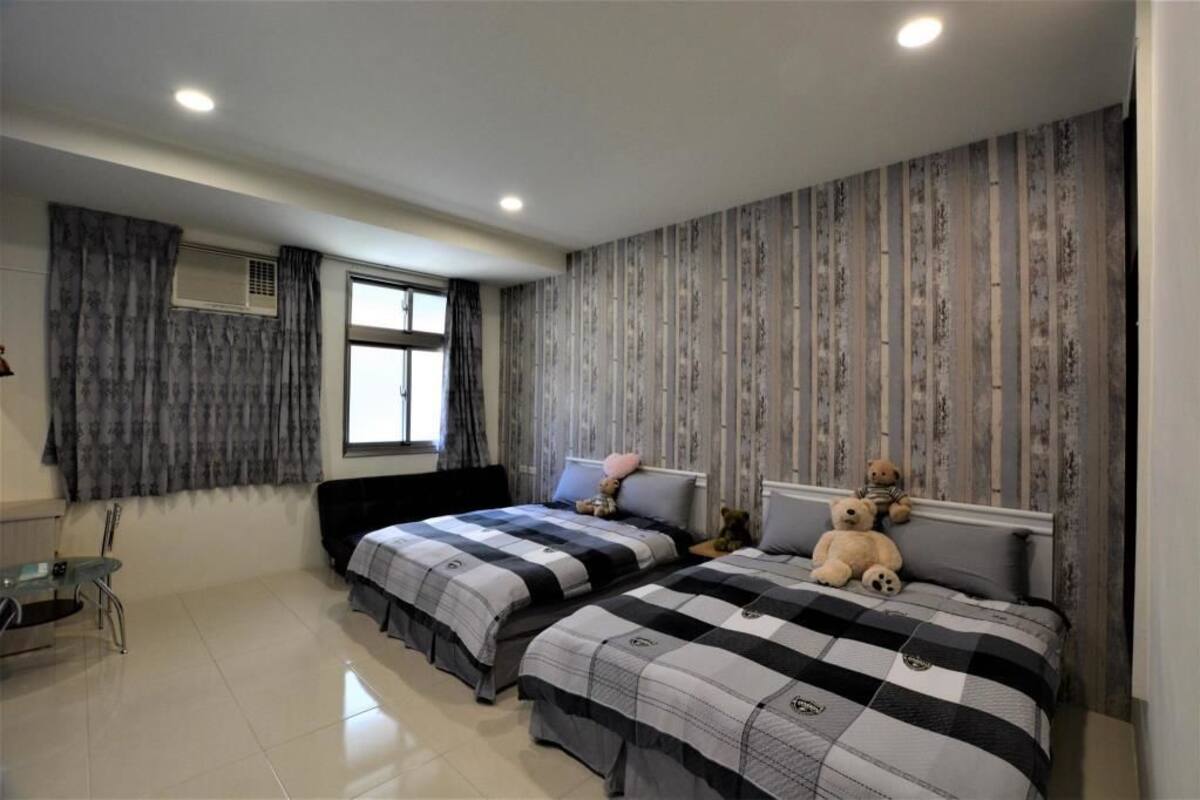 A bedroom with two beds, a window with curtains, a radiator, and a small table.