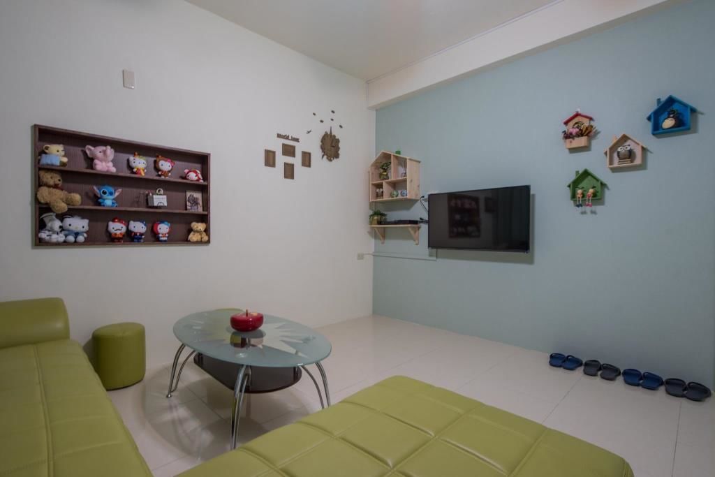 A living room with a sofa, a round coffee table, a TV, a shelf with stuffed toys, and a wall clock.