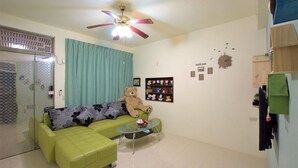 A living room with a green sofa, a glass coffee table, a teddy bear, a ceiling fan, and a wall with various decorations. - Tainan Jie Guo Inn (Tainan)