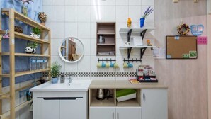 A kitchen with white cabinets, a wooden shelf with plants, a round mirror, and a corkboard with notes. - Tainan Jie Guo Inn (Tainan)