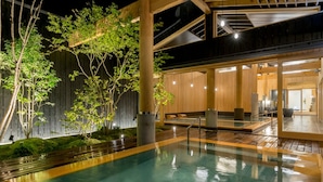 A modern indoor pool area with a wooden deck, a seating area, and a staircase leading to an upper level. - Awara Onsen Seifuso (Awara)
