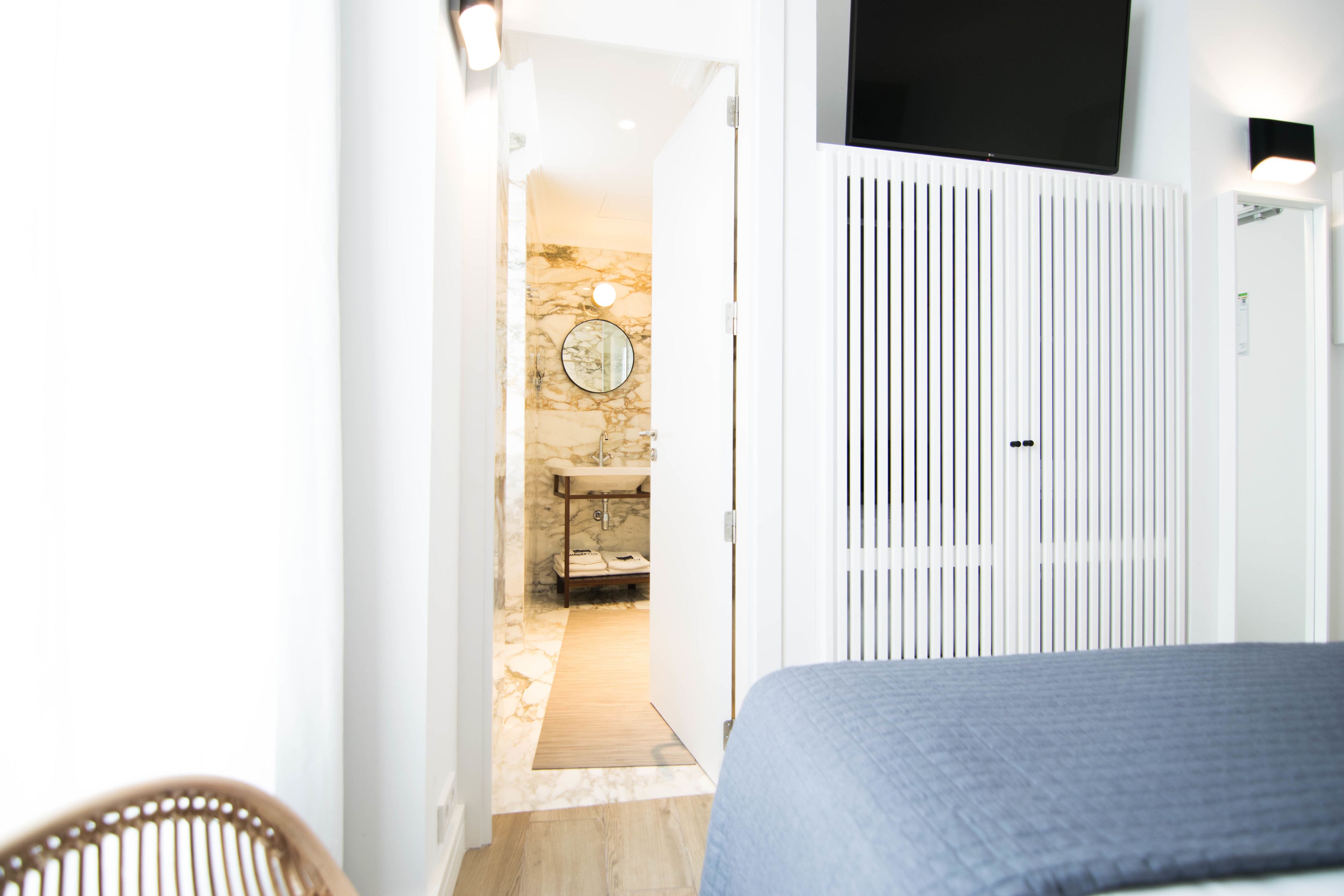 Un dormitorio con cama, un armario blanco, un baño con pared de mármol y un lavabo.