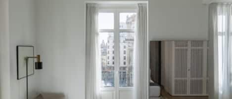 A modern hotel room with a large bed, a sofa, a view of the city through a window, and a wardrobe.