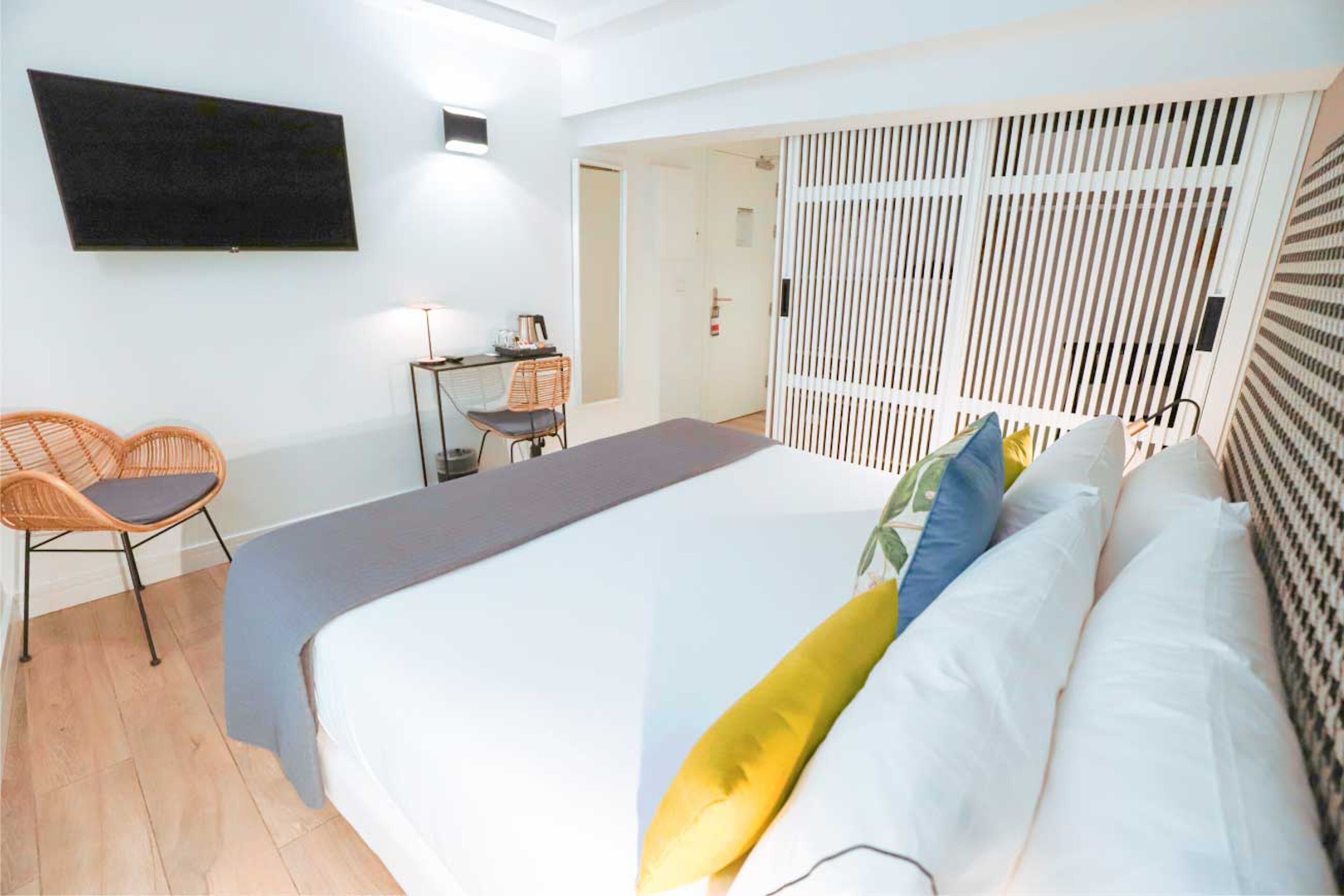 A modern hotel room with a large bed, a desk with a chair, a TV mounted on the wall, and a sliding door.