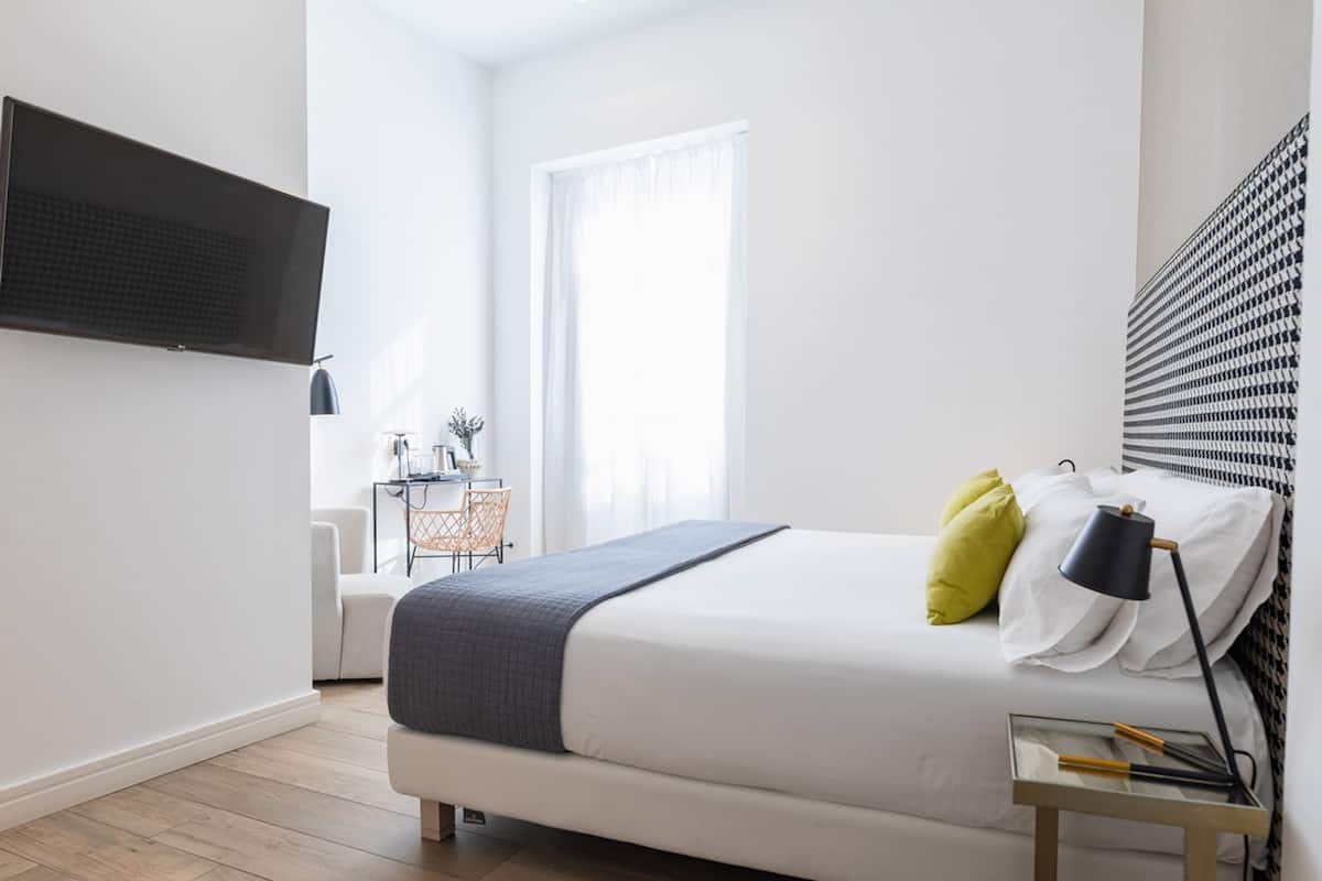 A modern bedroom with a large bed, a desk, and a TV mounted on the wall.