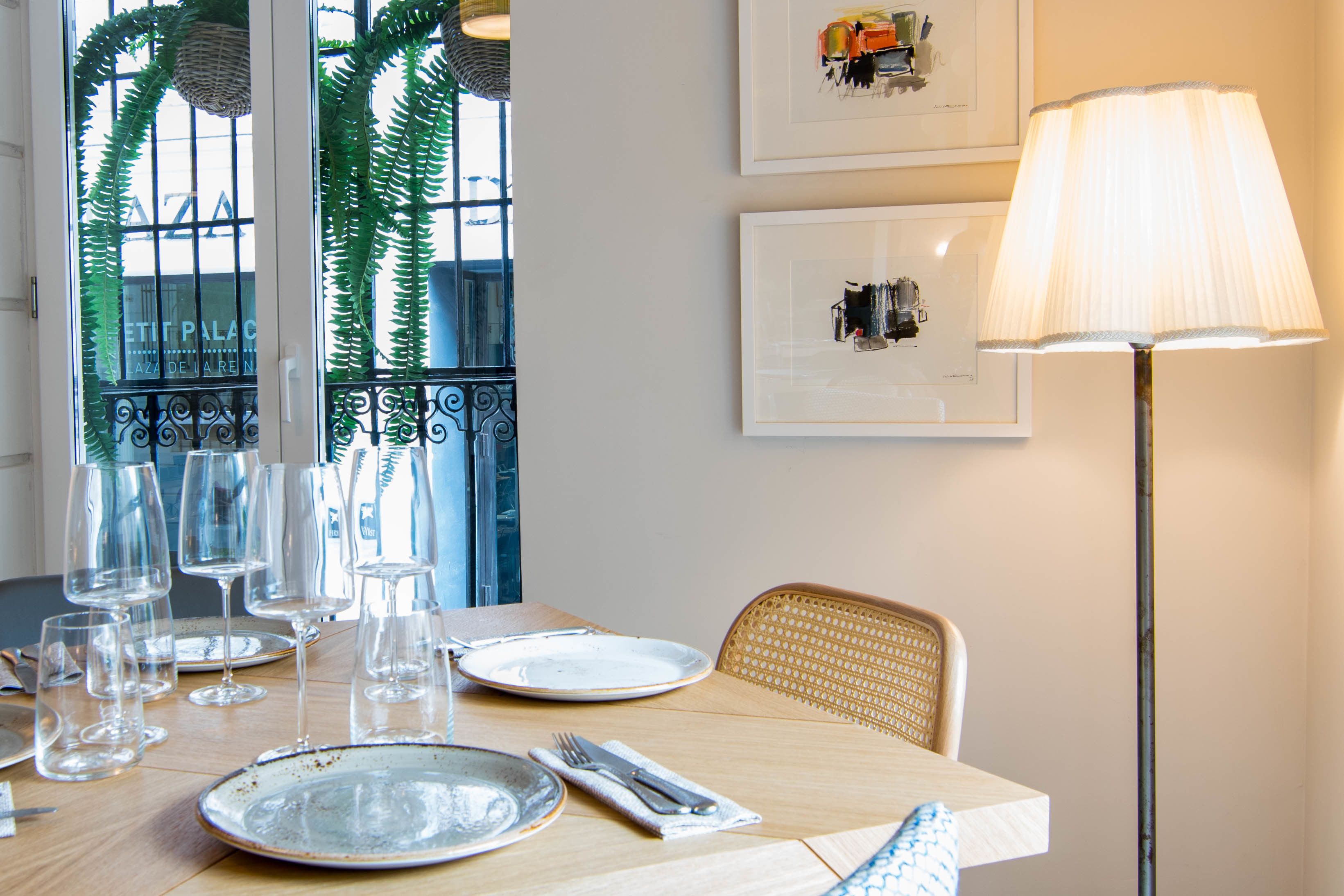 A dining table set with plates, glasses, and cutlery, a lamp, and framed artwork on the wall.