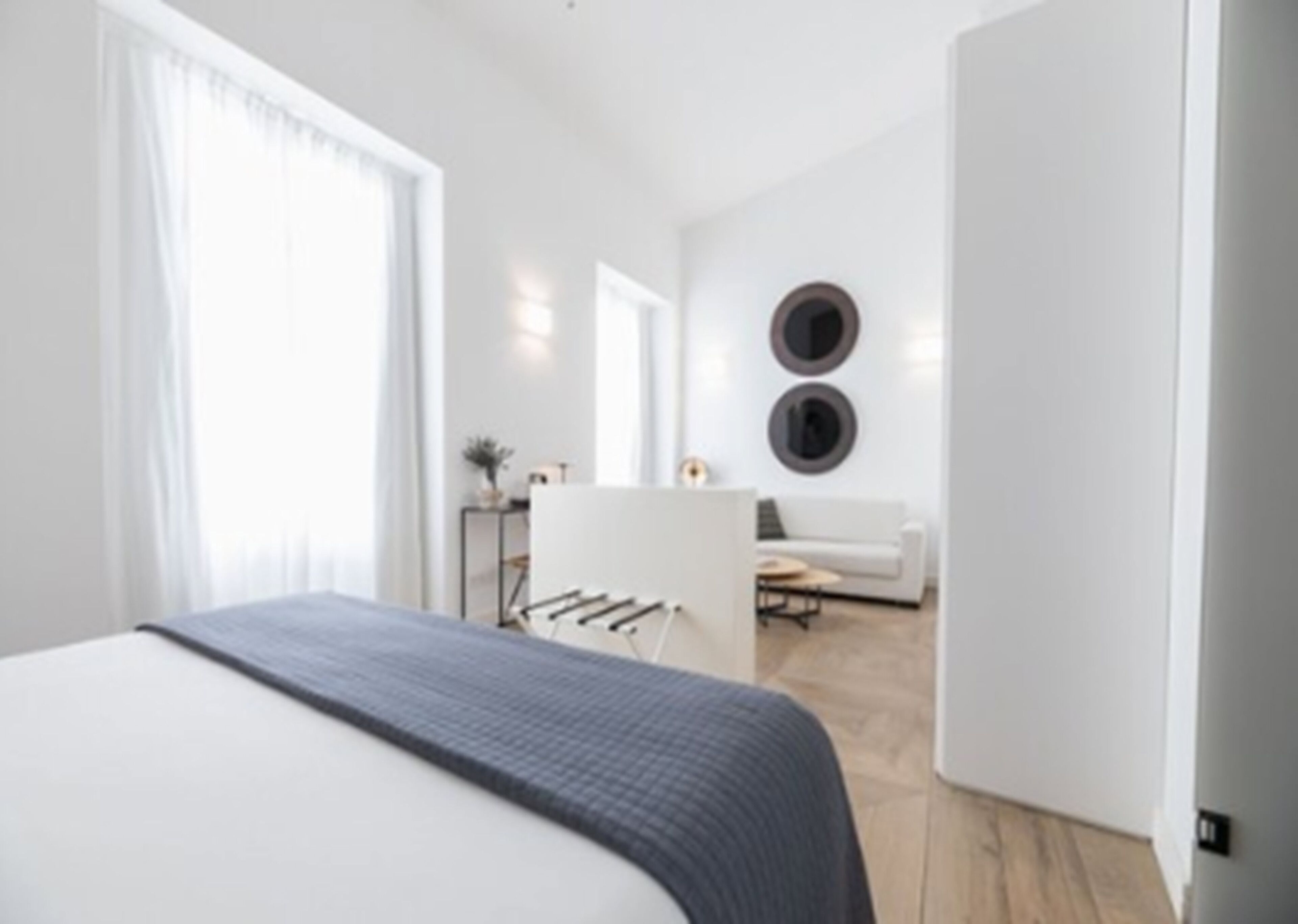 A modern bedroom with a large bed, a small desk, and a sofa in the background.