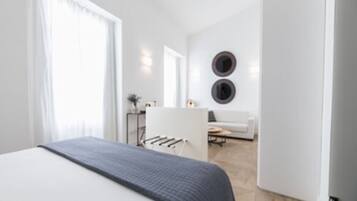 A modern bedroom with a large bed, a small desk, and a sofa in the background.