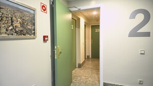 Un pasillo con paredes verdes, un cartel con el número 2, una puerta con pomo de latón y un cuadro con una vista urbana enmarcada.