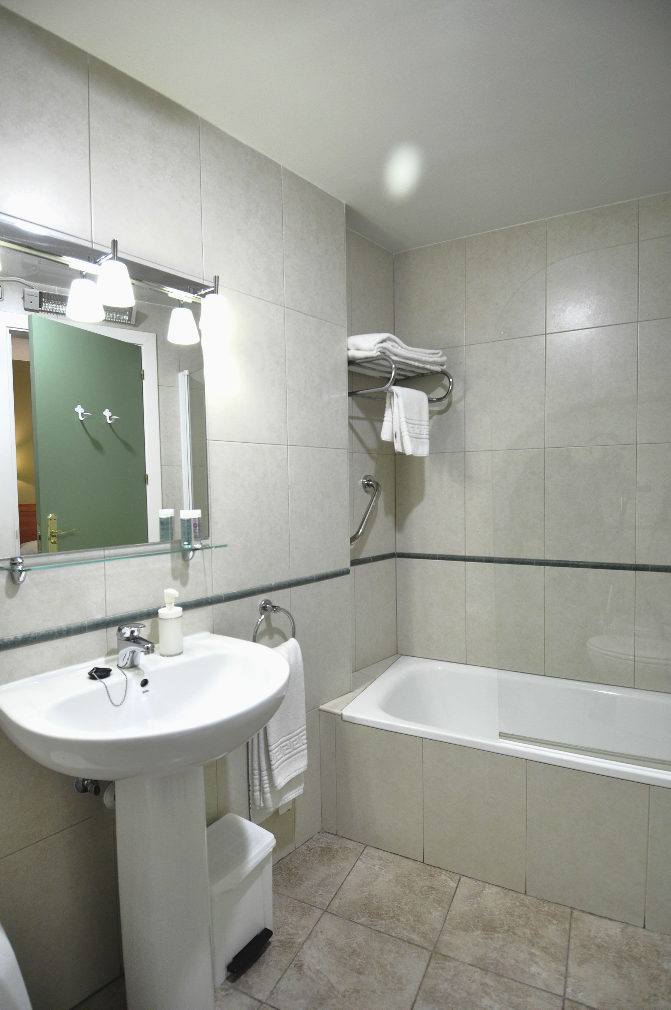 A bathroom with a sink, mirror, and bathtub. There is a towel rack above the bathtub and a glass shelf above the sink.