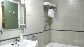 A bathroom with a sink, mirror, and bathtub. There is a towel rack above the bathtub and a glass shelf above the sink.