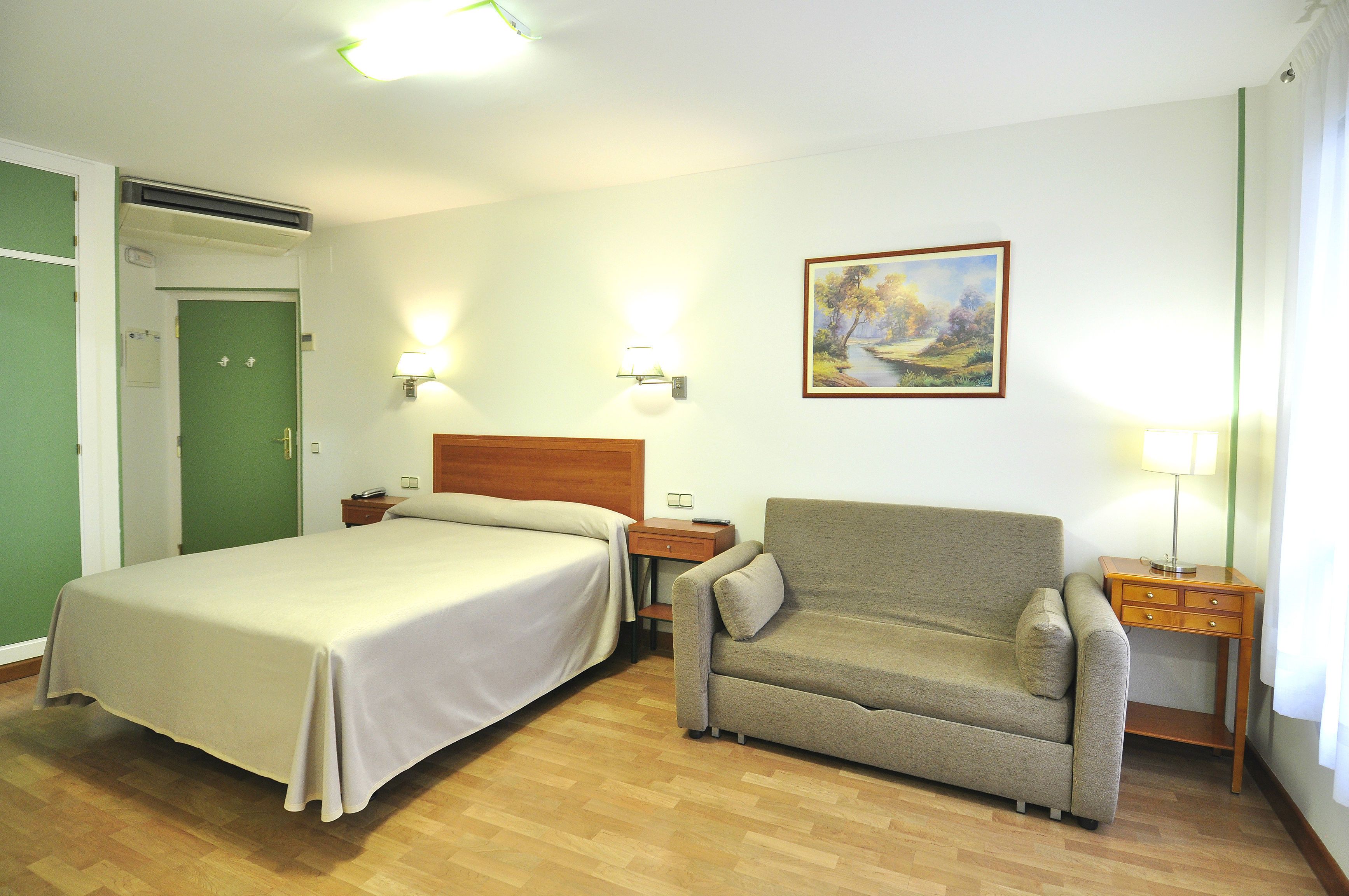 Una habitación de hotel con cama, sofá, mesita de noche y un cuadro en la pared.