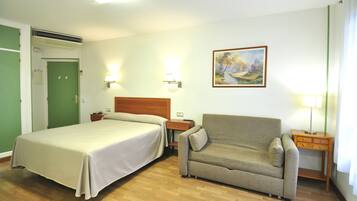 Una habitación de hotel con cama, sofá, mesita de noche y un cuadro en la pared.