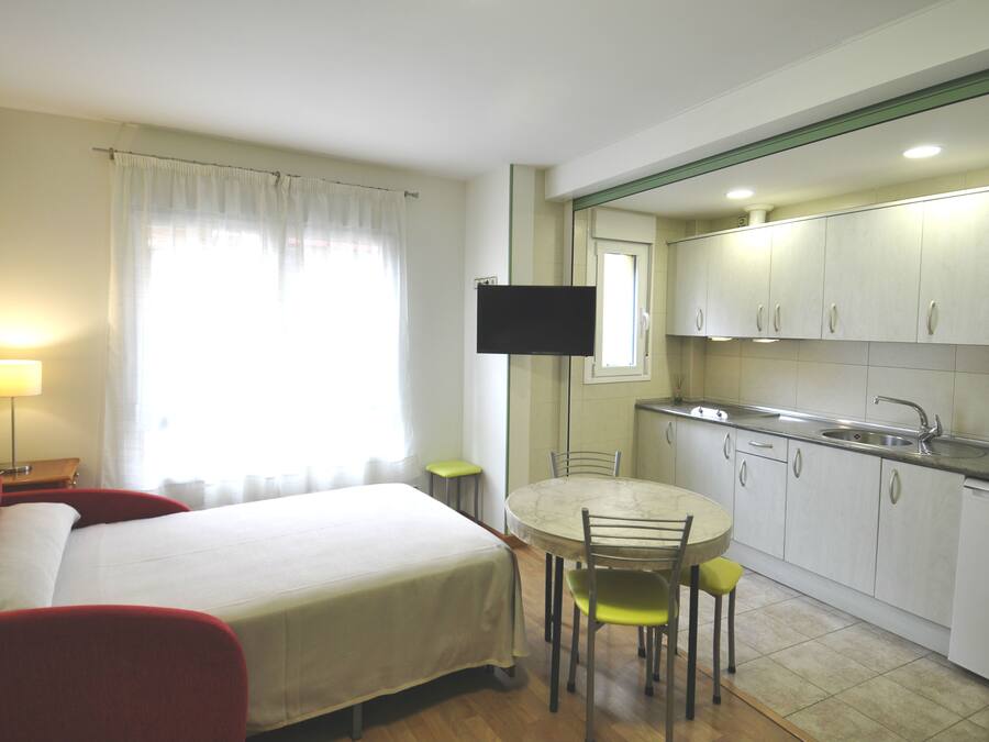 Une chambre d’hôtel comprenant un lit, une petite table avec des chaises, un coin cuisine avec des placards et un évier, ainsi qu’un téléviseur à écran plat fixé au mur.