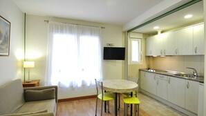 Un espacio habitable compacto con sofá, una mesa de comedor con sillas, un televisor de pantalla plana y una zona de cocina con armarios y fregadero.