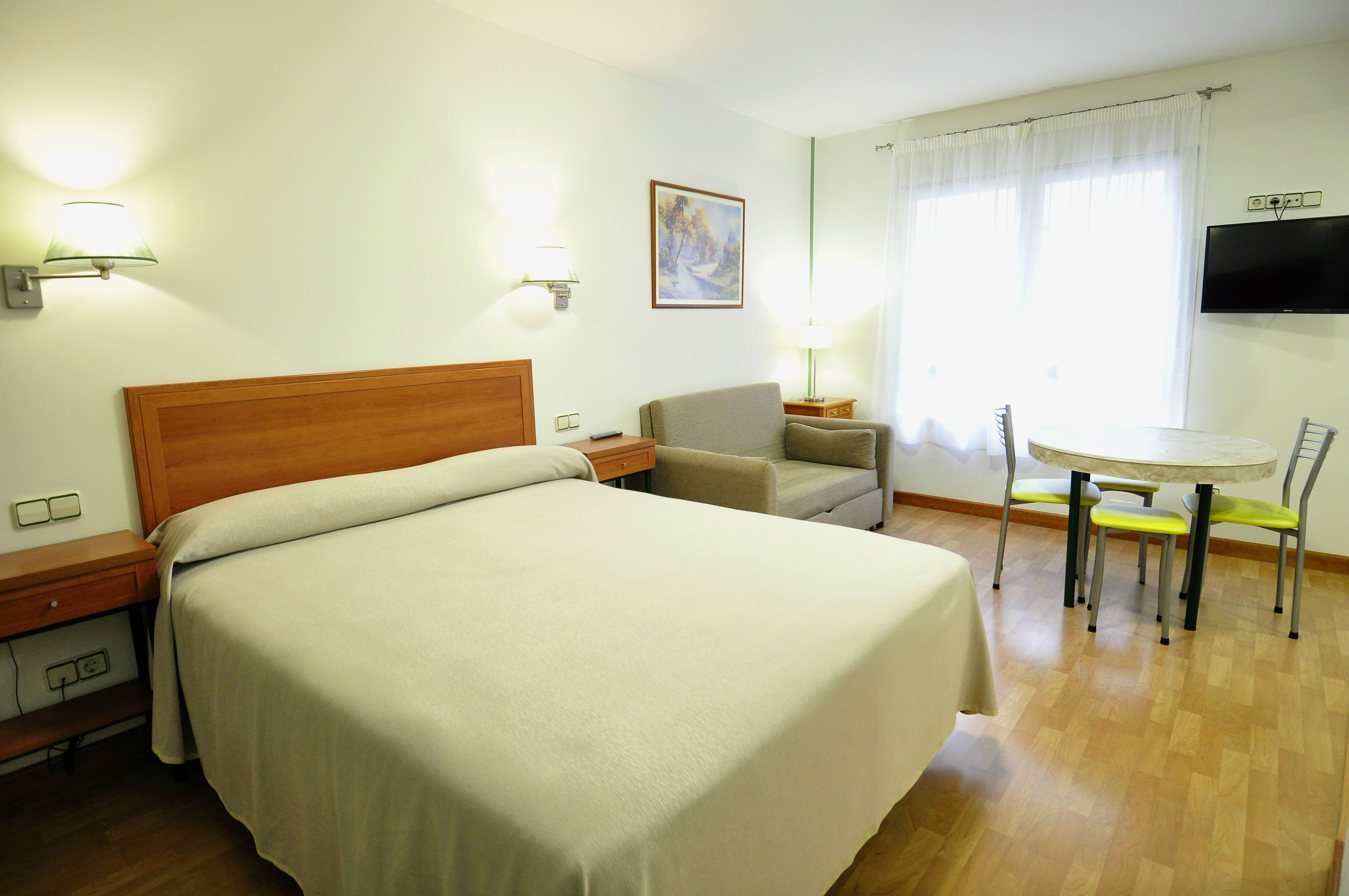 Habitació d'hotel amb un llit gran, un escriptori, una cadira, una taula petita i una televisió penjada a la paret.