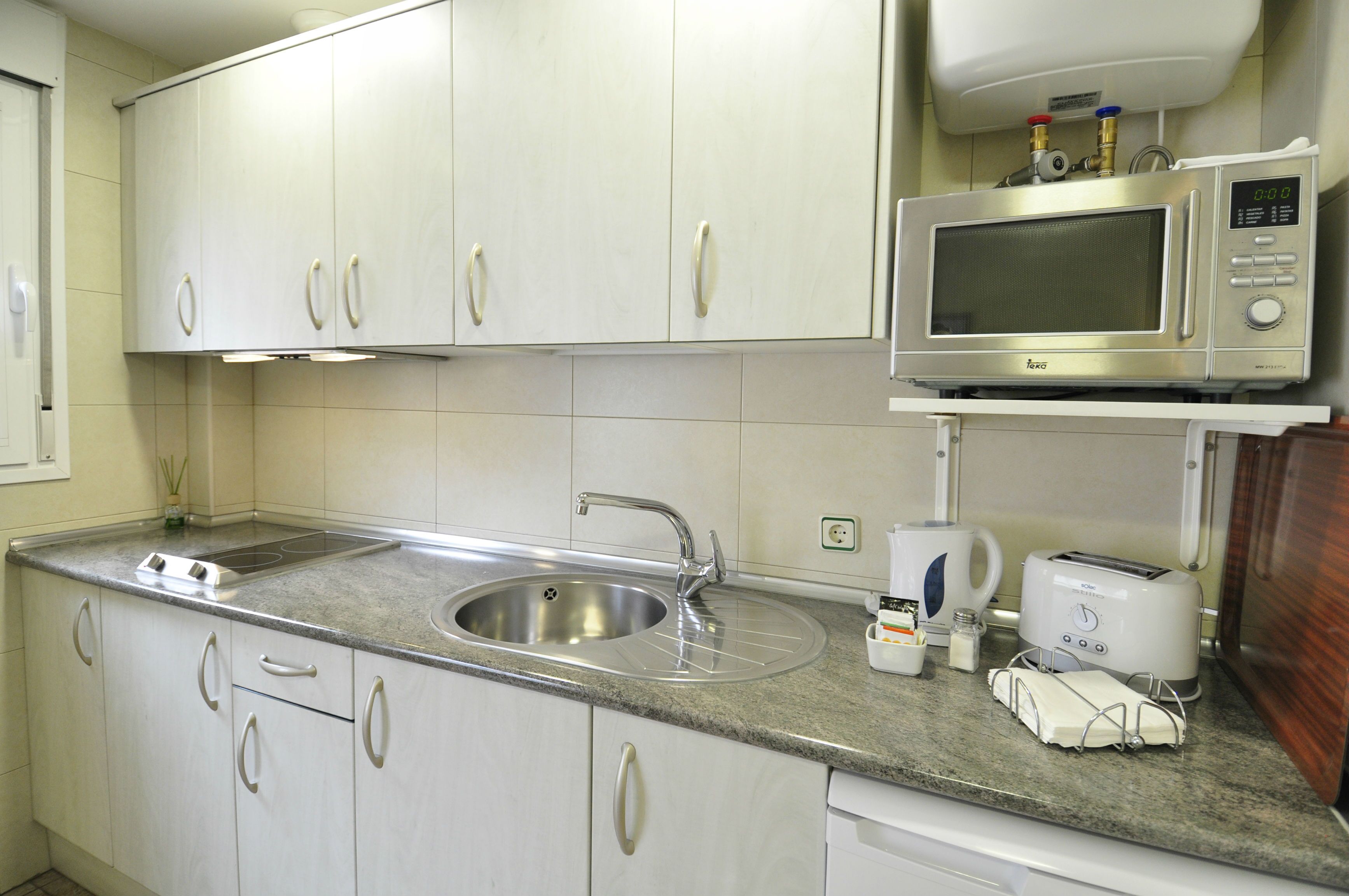 A kitchen with white cabinets, a stainless steel sink, a microwave, a toaster, and a coffee maker.